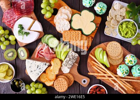 Scena di un tavolo di salumi a tema per il St Patricks Day su uno sfondo di legno. Varietà di antipasti a base di formaggio, carne, frutta e verdura. Vista dall'alto. Foto Stock