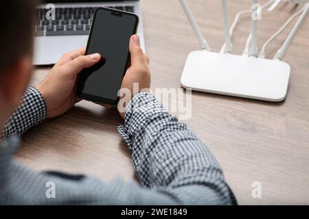 Uomo con smartphone e computer portatile che si connette a Internet tramite router Wi-Fi al tavolo di legno, primo piano Foto Stock