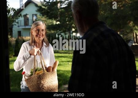 Aiutare i vicini. Donna anziana con sacchetto di prodotti in visita all'uomo all'aperto Foto Stock