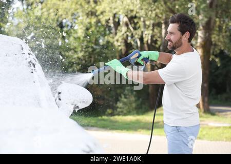 Uomo che copre l'automobile con schiuma all'autolavaggio esterno Foto Stock