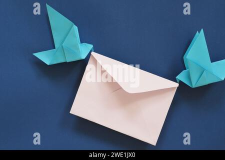 Due origami di carta da uccello che trasportano una busta di lettere. Ricezione e invio di e-mail e messaggi, corriere, servizio postale e concetto di consegna. Foto Stock