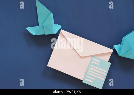 Due origami di carta da uccello che trasportano una busta di lettere. Ricezione di e-mail o messaggi di posta elettronica, ad esempio inviti e annunci o informazioni di memo. Foto Stock