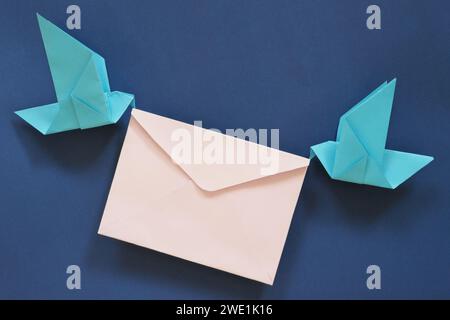 Due origami di carta da uccello che trasportano una busta di lettere. Ricezione e invio di e-mail e messaggi, corriere, servizio postale e concetto di consegna. Foto Stock