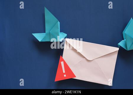 Due origami di carta per uccelli che trasportano una busta con un cartello di avvertimento. Truffa tramite e-mail di phishing e messaggio fraudolento. Foto Stock