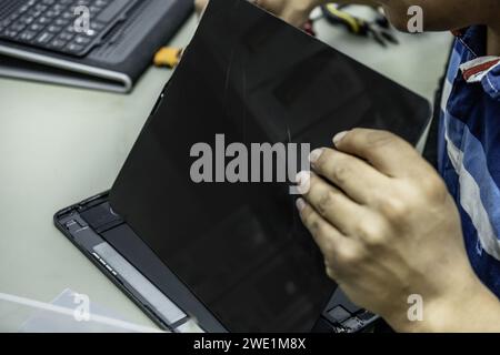 Un tecnico di un'officina di riparazione elettronica che avvita le parti su una riparazione dello schermo di un tablet Foto Stock