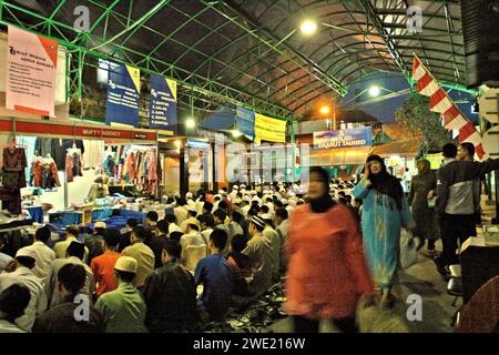 La gente cammina in uno spazio dietro la congregazione durante la preghiera del Maghrib in un centro commerciale situato di fronte alla moschea Daarut Tauhiid a Bandung, Giava Occidentale, Indonesia. Fondata da un famoso predicatore islamico indonesiano KH Abdullah Gymnastiar, dal collegio e dalla fondazione Daarut Tauhiid, insieme al suo marchio di attività Manajemen Qolbu (mq), sono riusciti a intensificare il turismo religioso e le attività economiche nell'area di Gegerkalong nella città di Bandung. Foto Stock