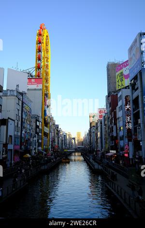 Vivace scena urbana dei canali a Dotonbori, Osaka, con annunci colorati e ruota panoramica contro il cielo azzurro. Foto Stock