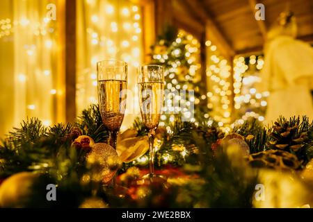 Due bicchieri di champagne ripieni di champagne sono collocati su un tavolo vicino all'albero di Natale. Gli occhiali sono circondati da luci che creano un'atmosfera festosa Foto Stock