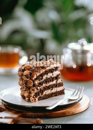 Torta stratificata estetica perfetta con caramello e noci sul piatto sopra il tavolo grigio. Pezzo di biscotto alle mandorle al cioccolato con glassa al caramello vicino alla tazza da tè e teiera infusa. Un pezzo di pan di Spagna nel caffè Foto Stock