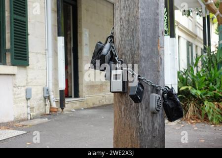 Sette cassette di sicurezza con serratura a combinazione su una catena intorno a un palo di legno sul sentiero per affittare un appartamento Airbnb a breve termine a Sydney Foto Stock