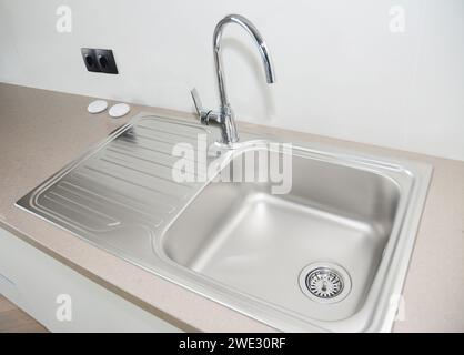 Ripiano da cucina con un moderno lavandino da cucina in metallo montato sulla parte superiore, rubinetto dell'acqua in acciaio inox e presa elettrica europea nera montata sul W Foto Stock