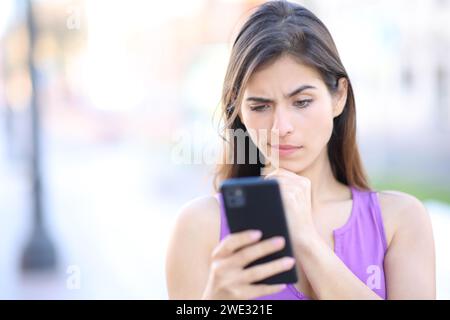 Vista frontale di una donna sospetta che controlla il telefono in strada Foto Stock
