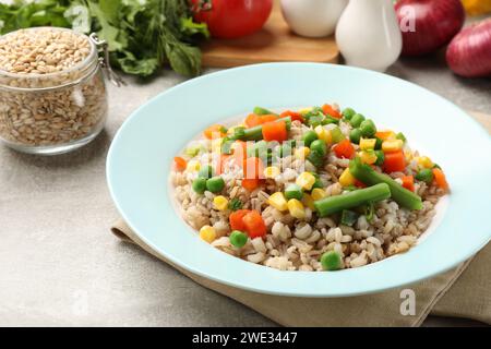 Saporito porridge di orzo perlato con verdure su un tavolo leggermente strutturato, primo piano Foto Stock