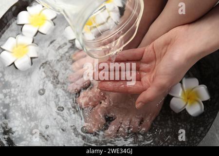 Donna che versa acqua sulla mano mentre immerge i piedi nella ciotola, sopra la vista. Trattamento spa Foto Stock