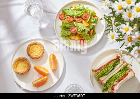 Colazione salutare per le persone che perdono peso, tenersi in forma con insalata fresca, panino, fetta d'arancia decorata su piatti bianchi rotondi e bicchiere d'acqua su W Foto Stock