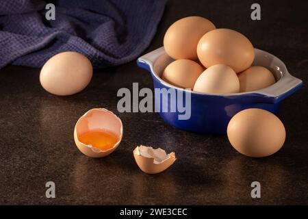 Primo piano di uova di gallina biologiche poste in una tazza blu su un rustico tavolo di legno scuro, creando una foto accattivante con illuminazione spettacolare. Foto Stock