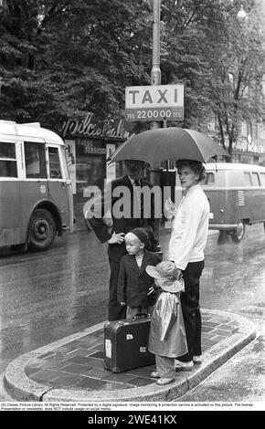 Stoccolma negli anni '1950 E' una giornata piovosa nel centro di Stoccolma. Una giovane coppia si trova sotto un ombrello in un palo di un taxi e aspetta un taxi, ma può essere una lunga attesa sotto l'ombrello per la giovane coppia con il tempo piovoso. Solo uno dei bambini indossa un impermeabile. Stoccolma 1953. Kristoffersson rif 2A-12 cv26-3 Foto Stock