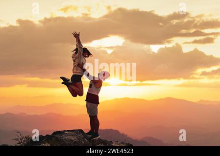 Le giovani coppie si divertono in cima alla montagna all'ora del tramonto. L'uomo sta lanciando una donna felice contro il cielo del tramonto Foto Stock