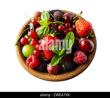 Bacche e frutta diverse in un recipiente. Bacche miste isolate in una ciotola di legno su sfondo bianco. Fragole, lamponi, gelsi, ribes rosso Foto Stock