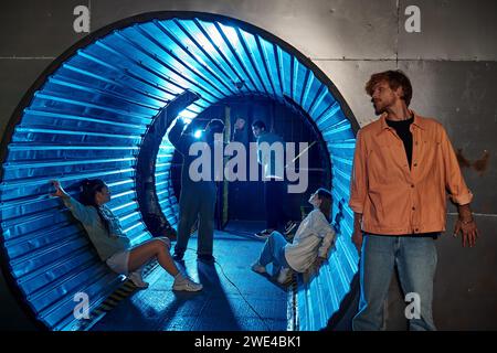 gruppo multietnico di amici che partecipano a un'emozionante avventura nella stanza delle missioni in un tunnel con luce blu Foto Stock