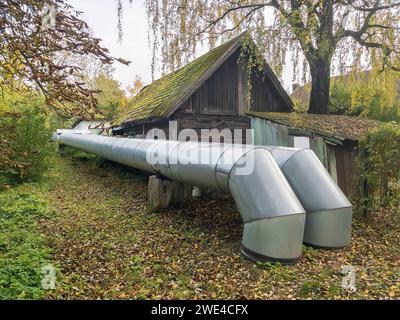 Due grandi tubi di calore all'aperto vicino alla vecchia casa di legno abbandonata in città. Foto Stock