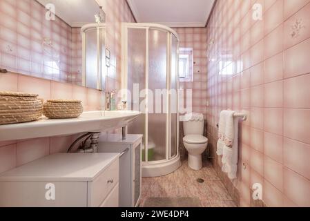 Un bagno con specchio rettangolare sospeso, lavandino dritto in porcellana sospesa, cabina doccia bianca e piastrelle rosa Foto Stock