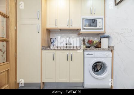 Una cucina tradizionale con mobili color crema con grandi triadi di metallo, elettrodomestici bianchi integrati e ripiano in granito porrino rosa Foto Stock