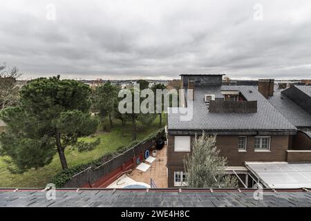 Tetti di un quartiere residenziale con piastrelle di ardesia nera accanto a un campo con erba e molti pini dolci Foto Stock