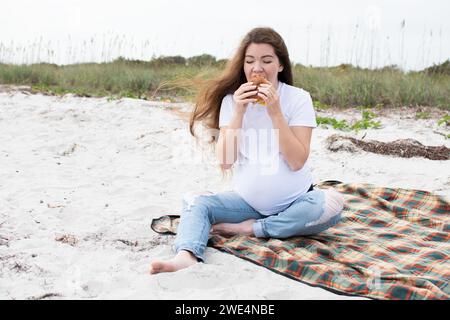 Donna incinta che mangia hamburger all'aperto. Mangiare durante la gravidanza. Concetto di dieta. Mangiare sano per la gravidanza Foto Stock