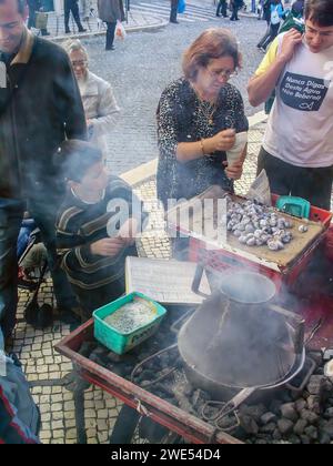 Lisbona, Portogallo: 10 novembre 2023: Venditore tradizionale di Castanhas Assadas o castagne arrosto e clienti felici. Tradizionale st Foto Stock