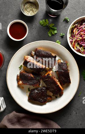 Costolette di maiale sul piatto su sfondo di pietra scura. Carne alla griglia servita con salsa e insalata di verdure fresche. Vista dall'alto, base piatta Foto Stock