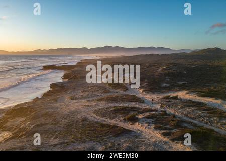 Vista aerea delle persone che cavalcano biciclette grasse al tramonto su sentieri sabbiosi lungo la costa e la spiaggia nella riserva naturale di Walker Bay, Gansbaai De Kelders, W. Foto Stock