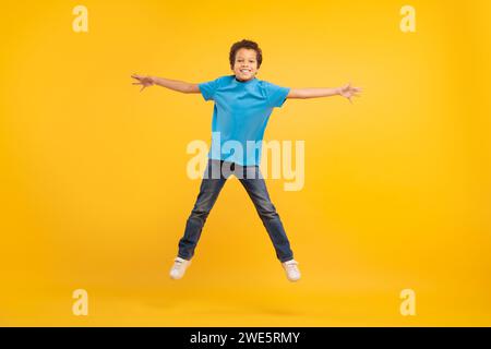 Ragazzo gioioso che salta con le braccia tese, sfondo giallo Foto Stock