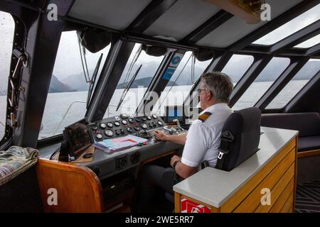 Capitano della nave che guida un traghetto passeggeri in catamarano Realnz sul lago Manapouri, Aotearoa (nuova Zelanda), te Waipounamu (Isola del Sud) Foto Stock