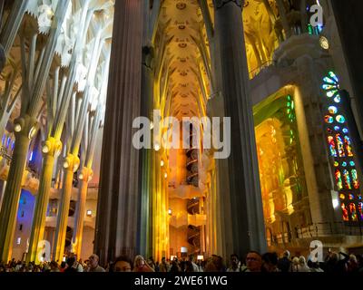 I turisti all'interno della basilica della Sagrada Familia ammirano la luce colorata che passa attraverso le vetrate colorate Foto Stock