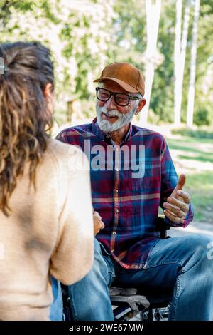 Uomo anziano felice in sedia a rotelle che parla con l'operatore sanitario Foto Stock