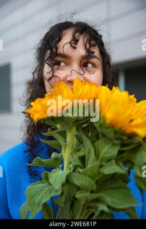 Giovane donna con i capelli ricci che odora i girasoli Foto Stock