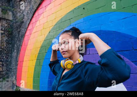 Giovane donna che flessa i muscoli davanti alla parete dell'arcobaleno Foto Stock