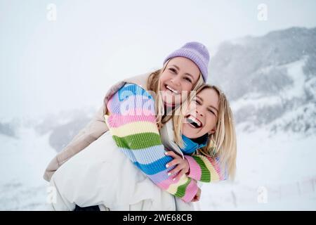 Una felice donna bionda che fa un giro in piggyback ad un amico su una montagna innevata sotto il cielo Foto Stock