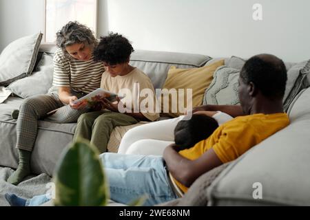 Madre con figlio che guarda il disegno e padre che coccola sua figlia seduta sul divano Foto Stock