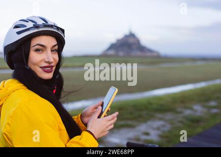 Donna sorridente che indossa un casco da ciclismo con smartphone Foto Stock