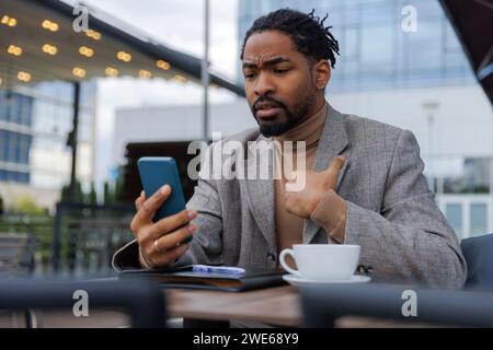 Un uomo d'affari scontento che parla in videochiamata tramite smartphone al bar Foto Stock