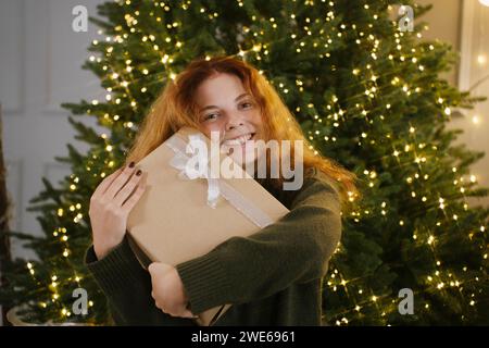 Donna felice che tiene una confezione regalo vicino all'albero di Natale Foto Stock