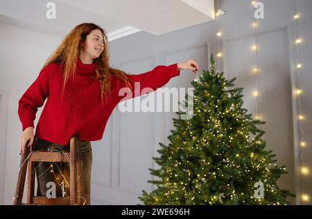 Donna rossa sorridente che decora l'albero di Natale a casa Foto Stock
