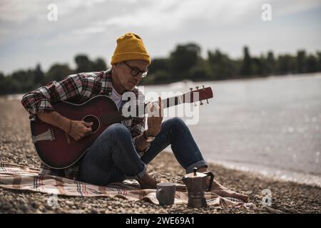 Anziano che suona la chitarra seduto al mare nel fine settimana Foto Stock