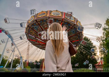 Donna bionda che raggiunge la giostra nel parco divertimenti al tramonto Foto Stock