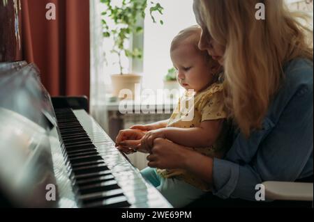 Madre insegnando a figlia di suonare il pianoforte a casa Foto Stock