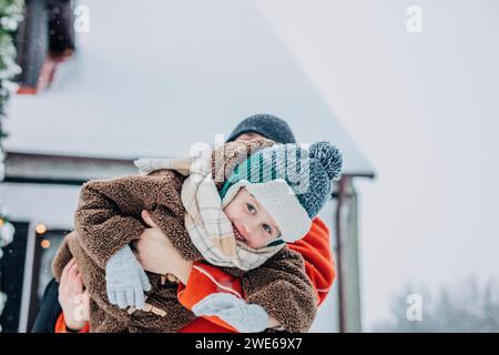 Ragazzo sorridente in braccio al padre in una giornata nevosa Foto Stock