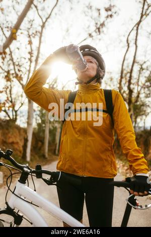 Donna che beve acqua da una bottiglia vicino alla mountain bike nella foresta Foto Stock