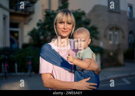 Donna sorridente che porta un figlio in una fionda Foto Stock